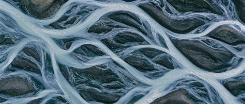 Aerial top-down view of a braided glacial river delta flowing over dark rocky terrain in Iceland