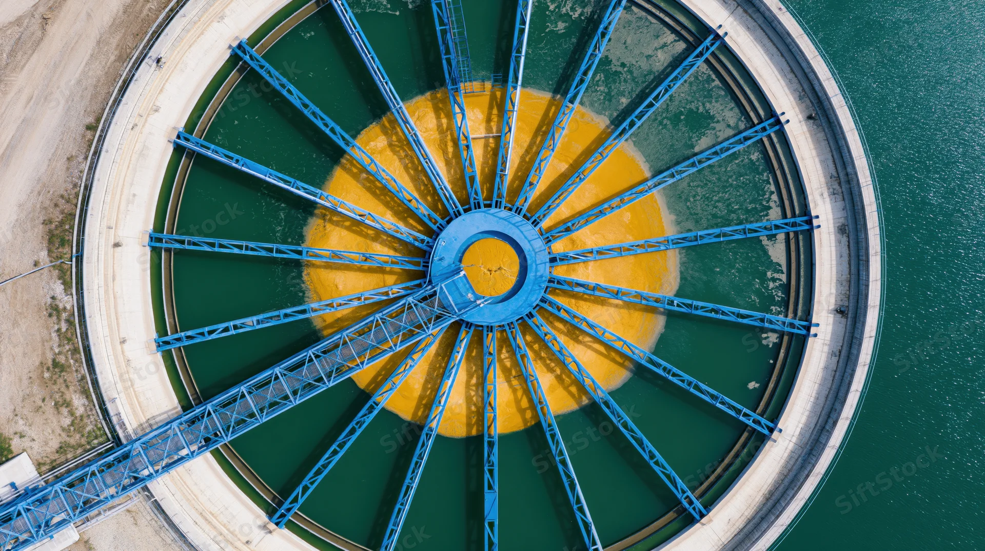 Aerial top-down view of a circular water treatment clarifier with blue radial beams and yellow center in a green water tank