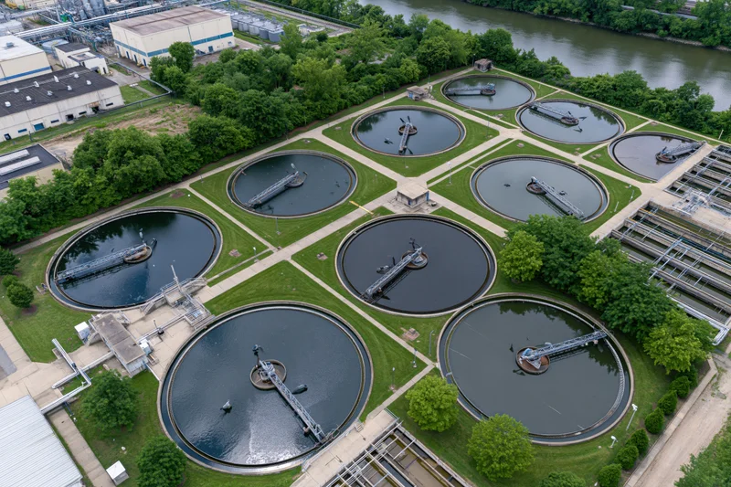 Aerial top-down view of a municipal water treatment facility with circular clarifier tanks and surrounding greenery