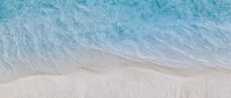 Aerial top-down view of a wave breaking onto pale cream sand at a shallow shoreline