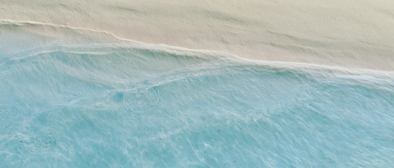 Aerial top-down view of shallow ocean waves meeting pale cream sand at shoreline