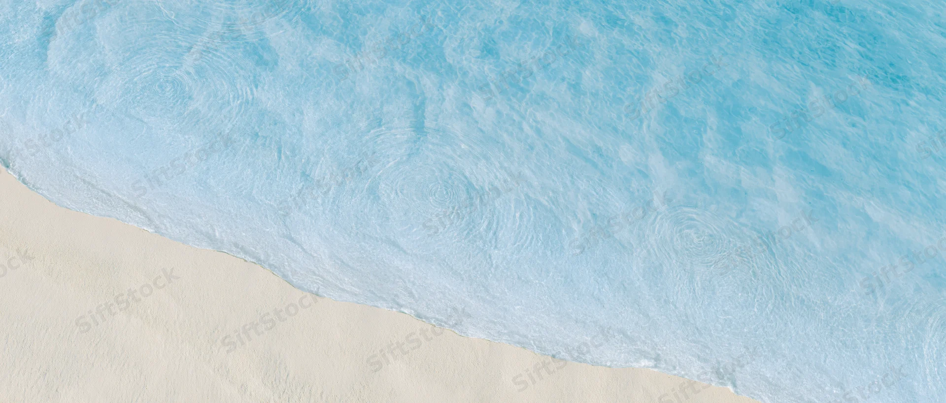 Aerial top-down view of shallow ocean water meeting pale cream sand at shoreline