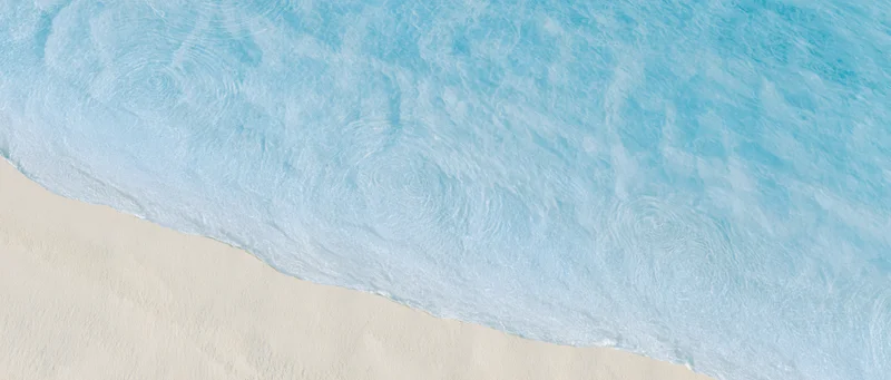 Aerial top-down view of shallow ocean water meeting pale cream sand at shoreline