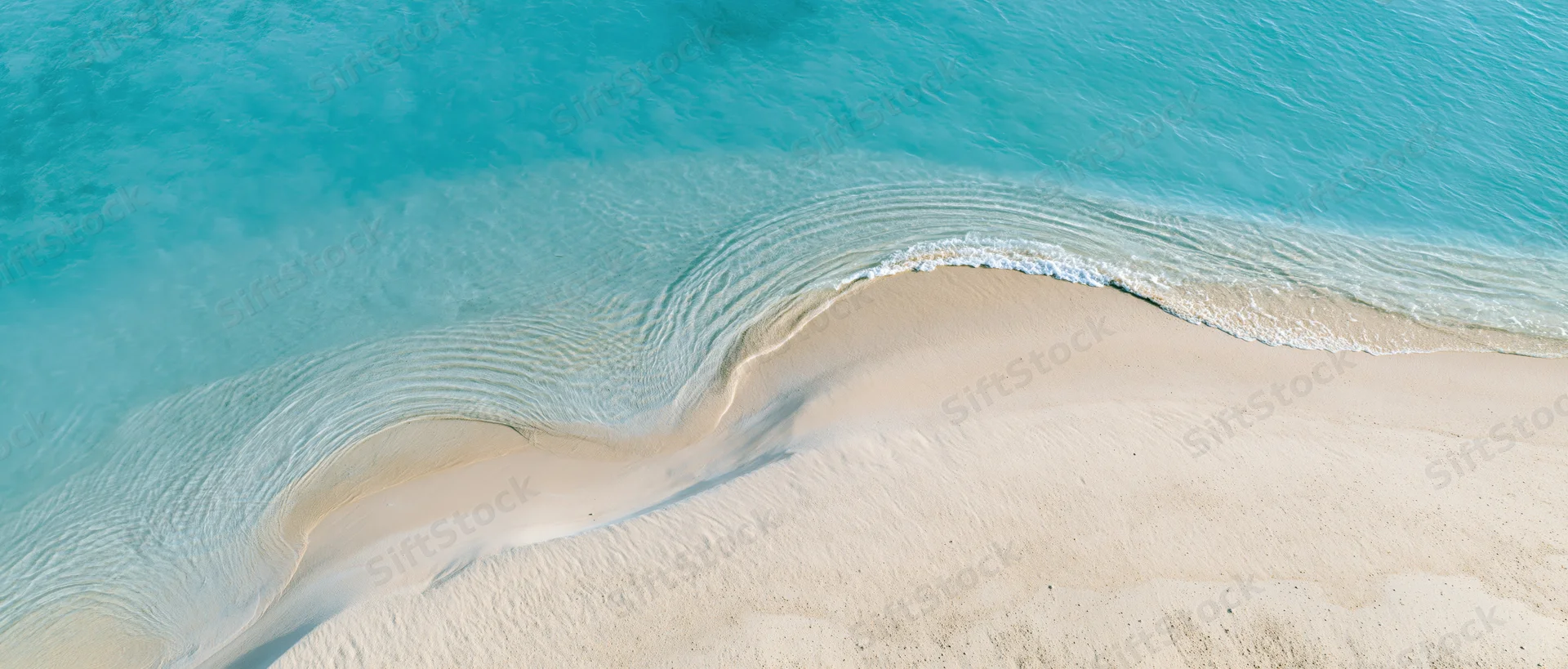 Aerial top-down view of a shallow tropical shoreline with turquoise water meeting white sand