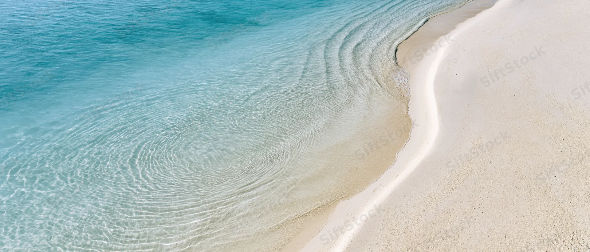 Aerial top-down view of a shallow tropical shoreline with clear turquoise water meeting white sand