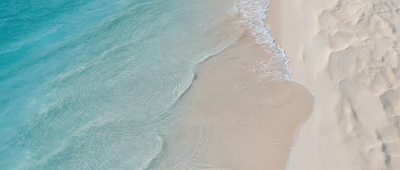 Aerial top-down view of turquoise ocean waves meeting white sand shoreline