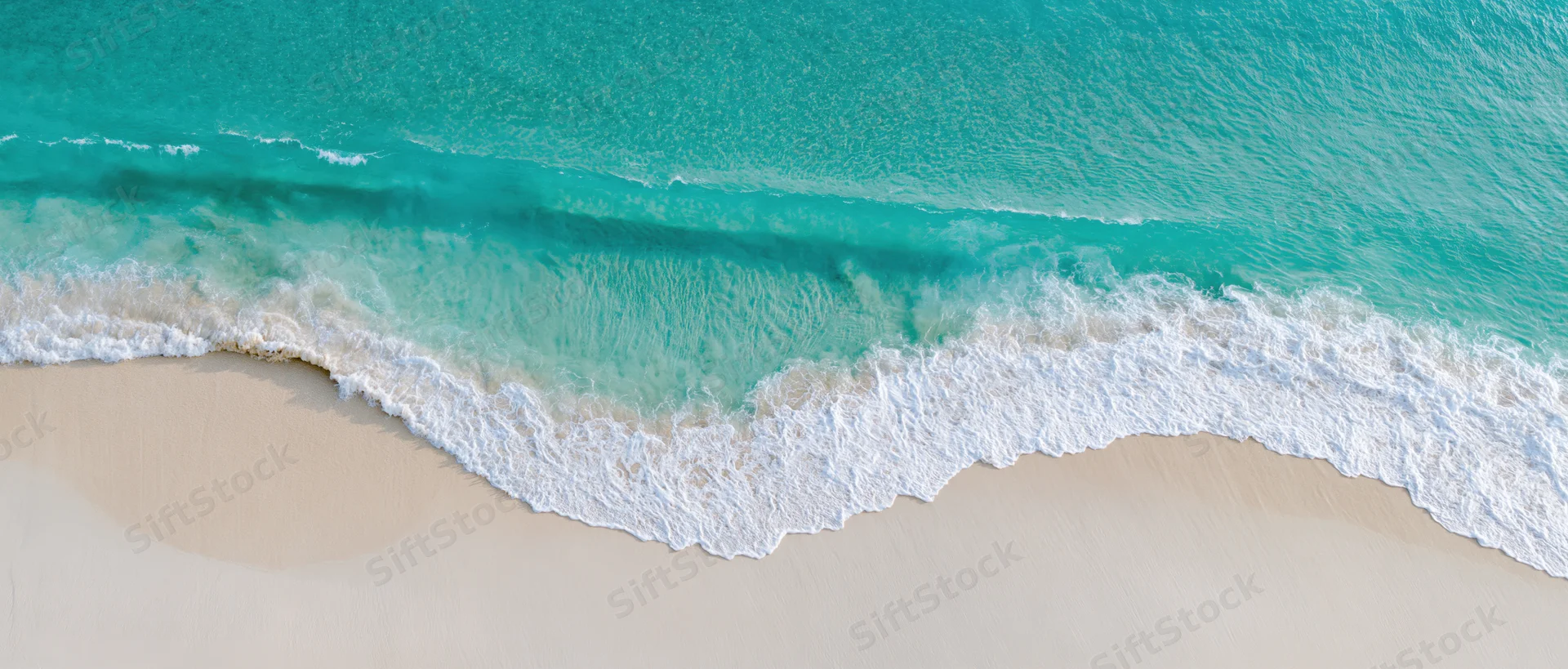 Aerial top-down view of turquoise ocean wave gently breaking on sandy beach