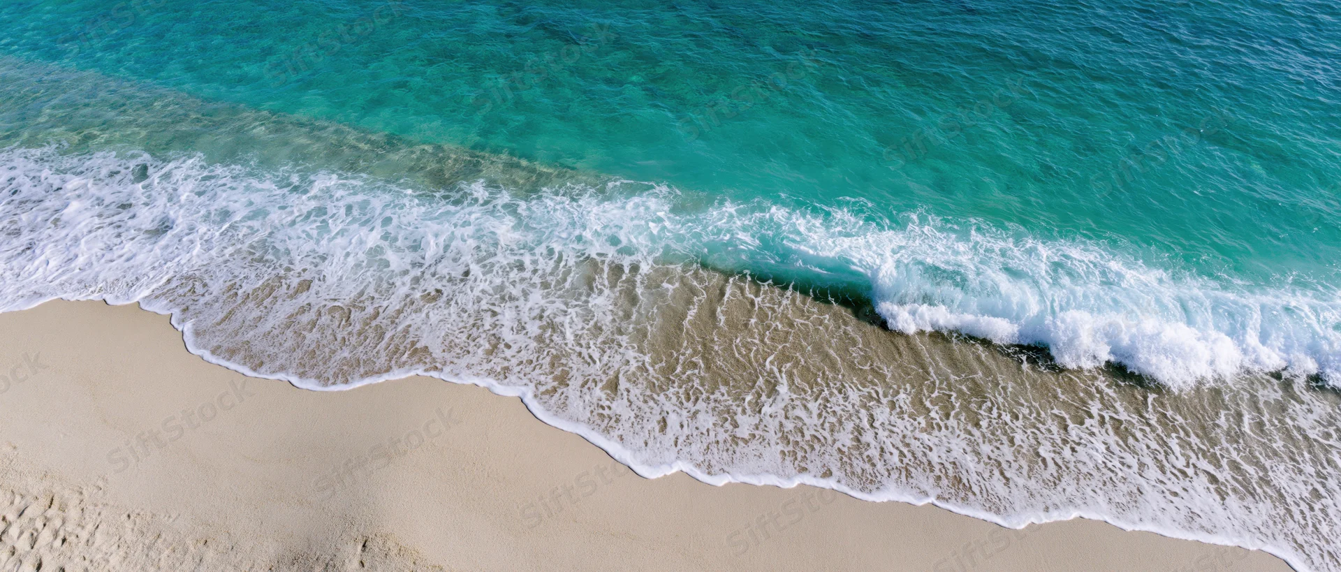 Aerial top-down view of turquoise ocean wave meeting sandy beach