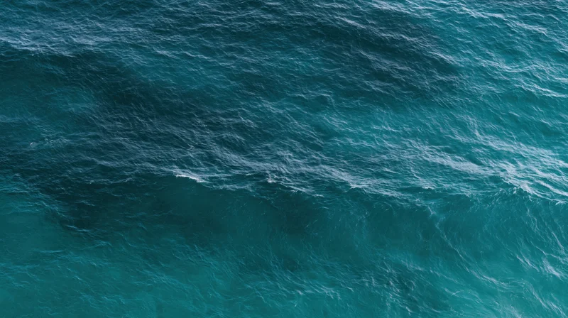Aerial top-down view of open ocean surface with rippling waves and varying blue tones