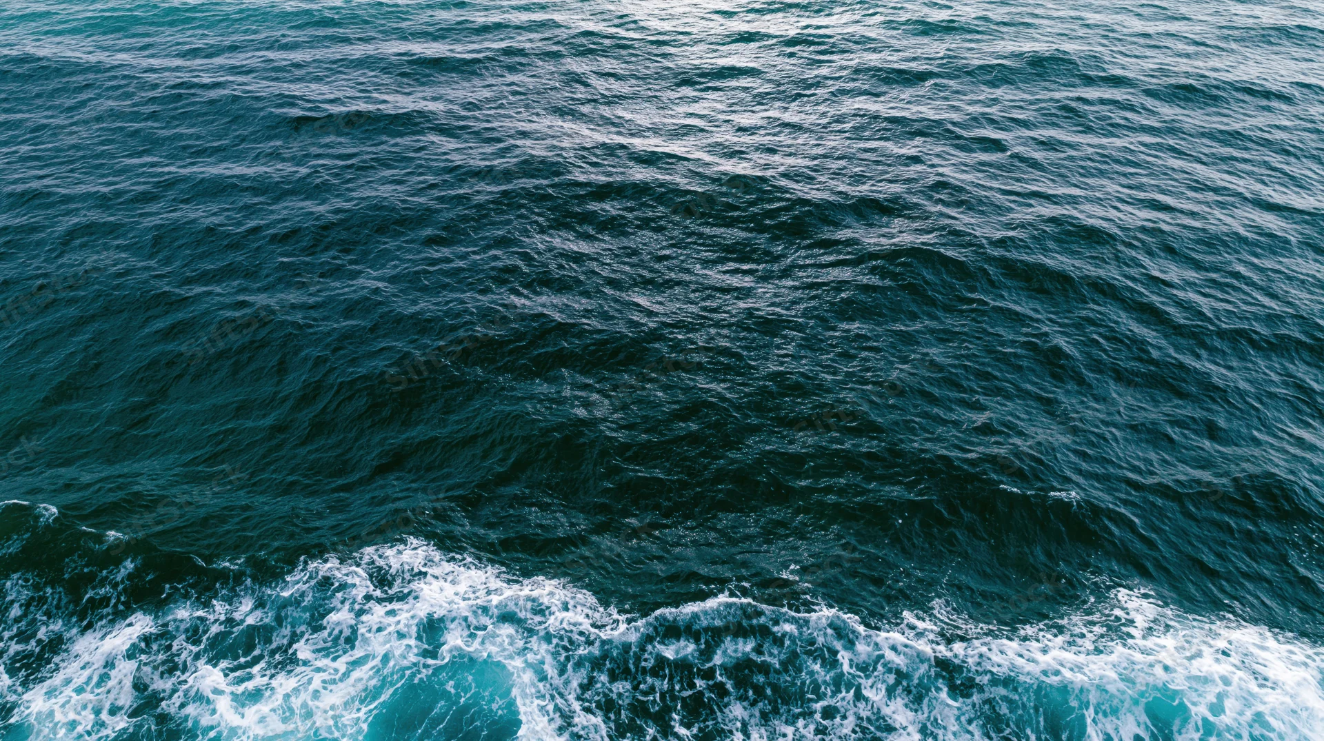 Aerial top-down view of open ocean surface with small ripples and white foam along the edge