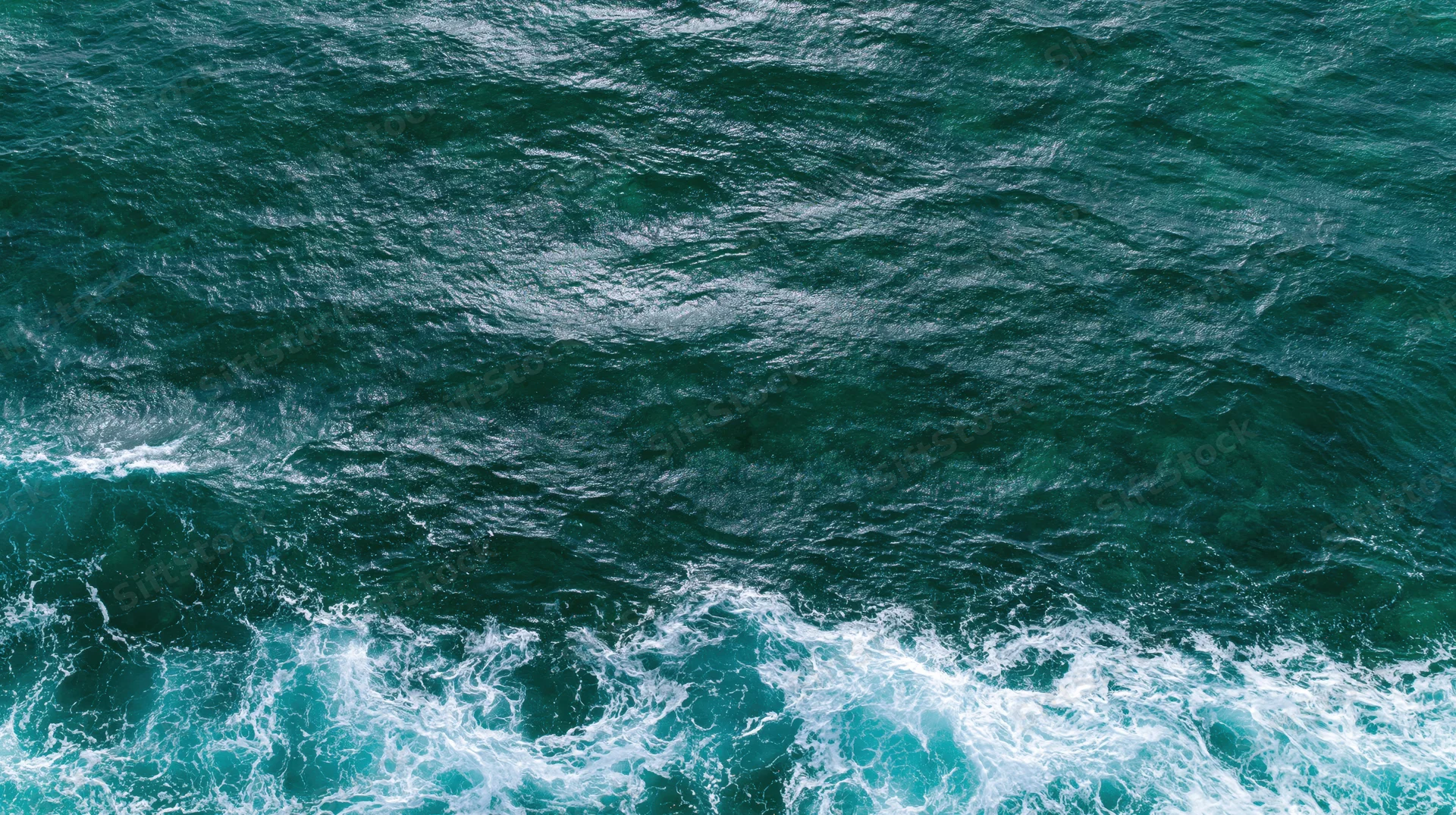 Aerial top-down view of ocean surface with rippling waves and white foam along the edge