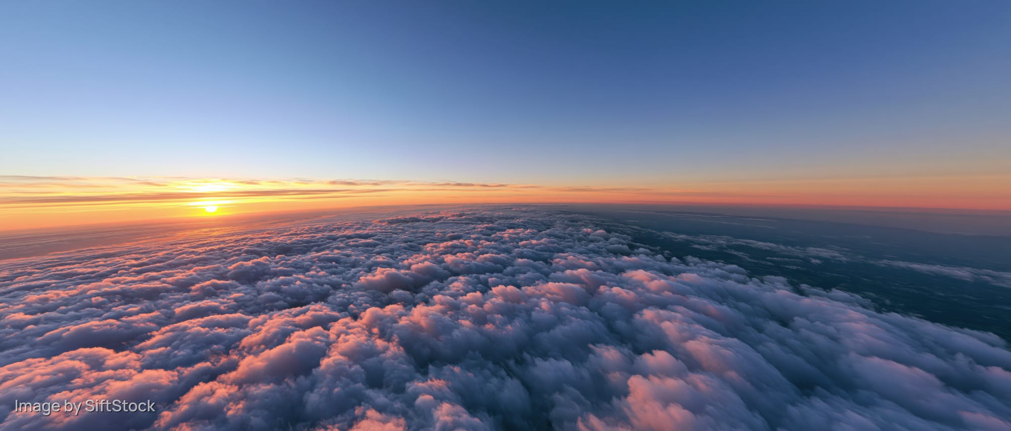Aerial view above dense cloud layer at sunrise with sun on horizon