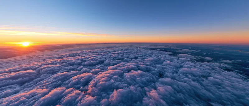 Aerial view above dense cloud layer at sunrise with sun on horizon