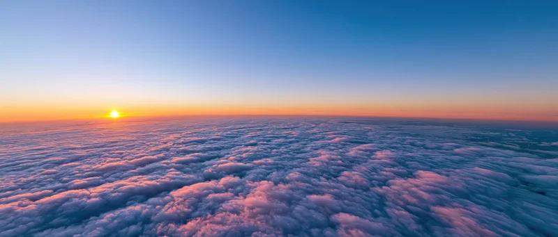 Aerial view above dense cloud layer at sunrise with orange and blue sky