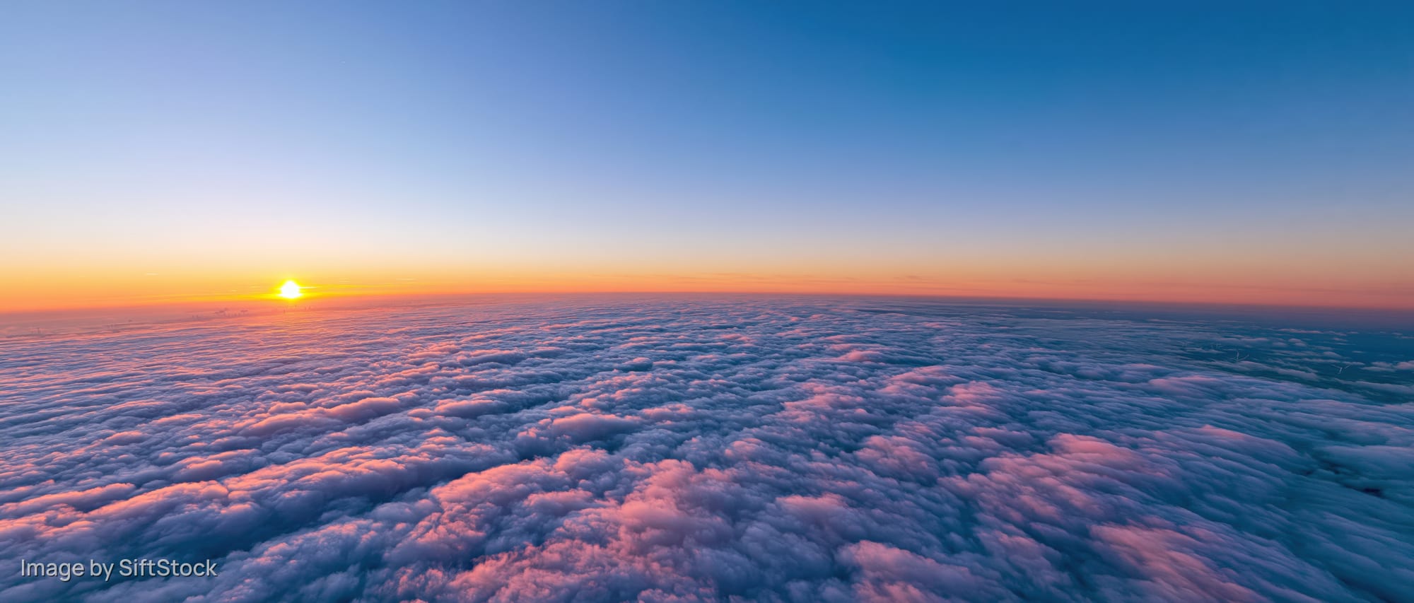 Aerial view above dense cloud layer at sunrise with orange and blue sky