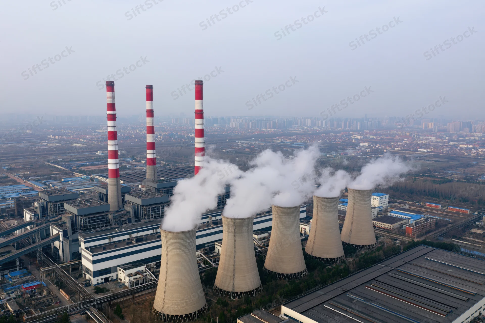 Aerial view of a coal-fired power plant with cooling towers emitting steam and smoke over an urban landscape