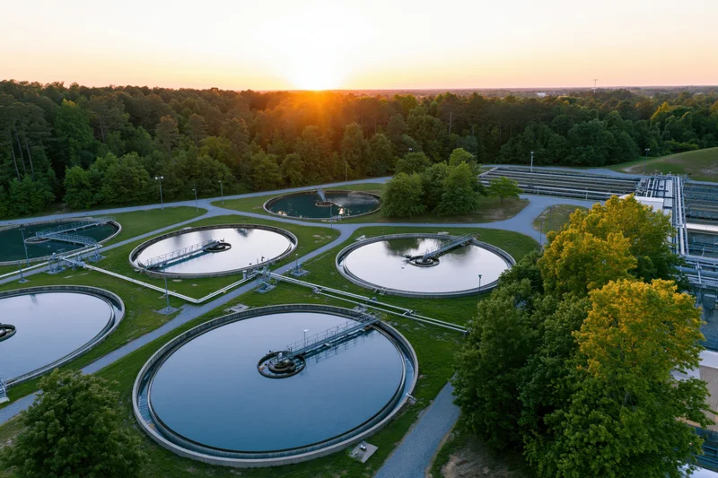 Aerial view of circular wastewater treatment tanks surrounded by trees at sunset