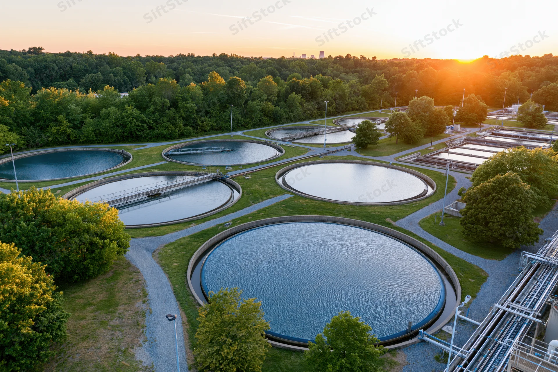 Aerial view of circular wastewater treatment tanks surrounded by greenery at sunset