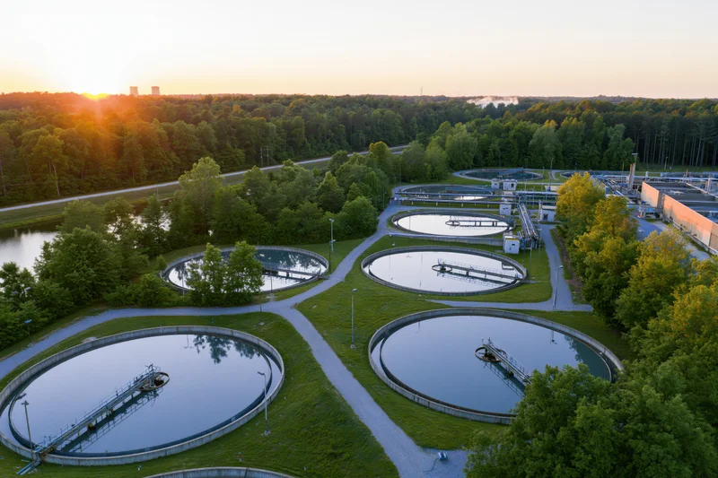 Aerial view of circular wastewater treatment tanks surrounded by greenery and trees at sunset
