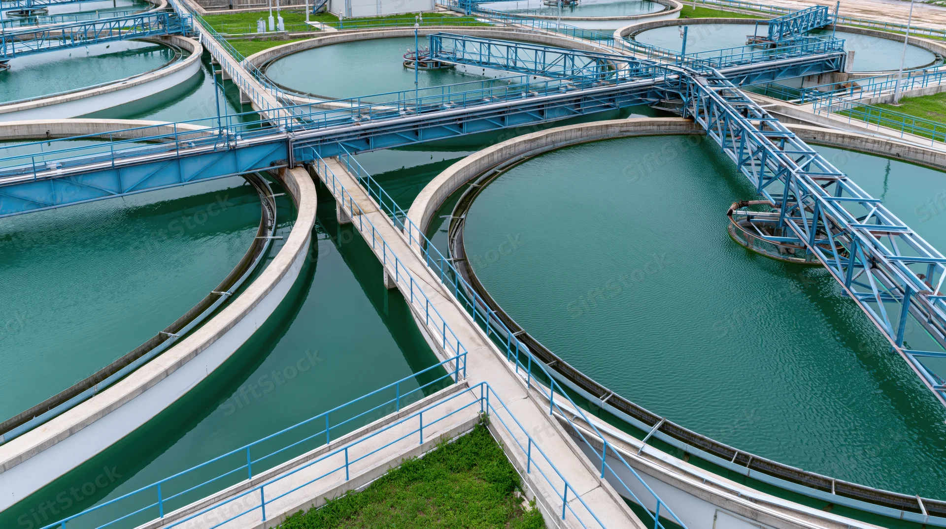 Aerial view of circular tanks in a wastewater treatment plant with blue metal walkways and green water