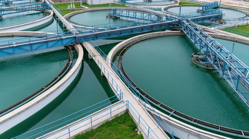 Aerial view of circular tanks in a wastewater treatment plant with blue metal walkways and green water