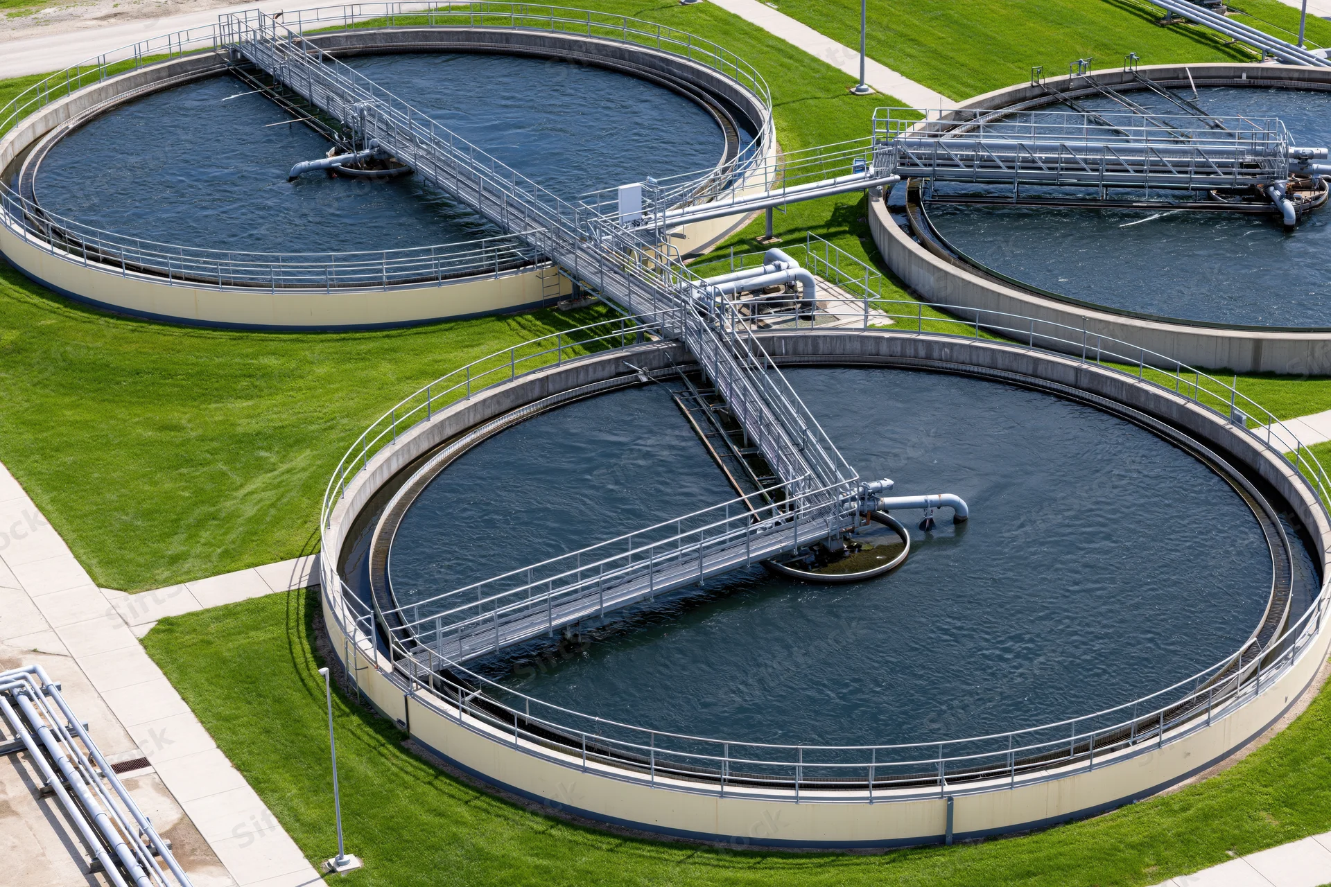 Aerial view of three circular wastewater treatment tanks with metal walkways and pipes at a municipal facility