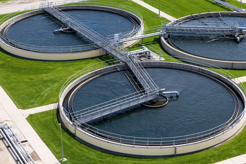 Aerial view of three circular wastewater treatment tanks with metal walkways and pipes at a municipal facility