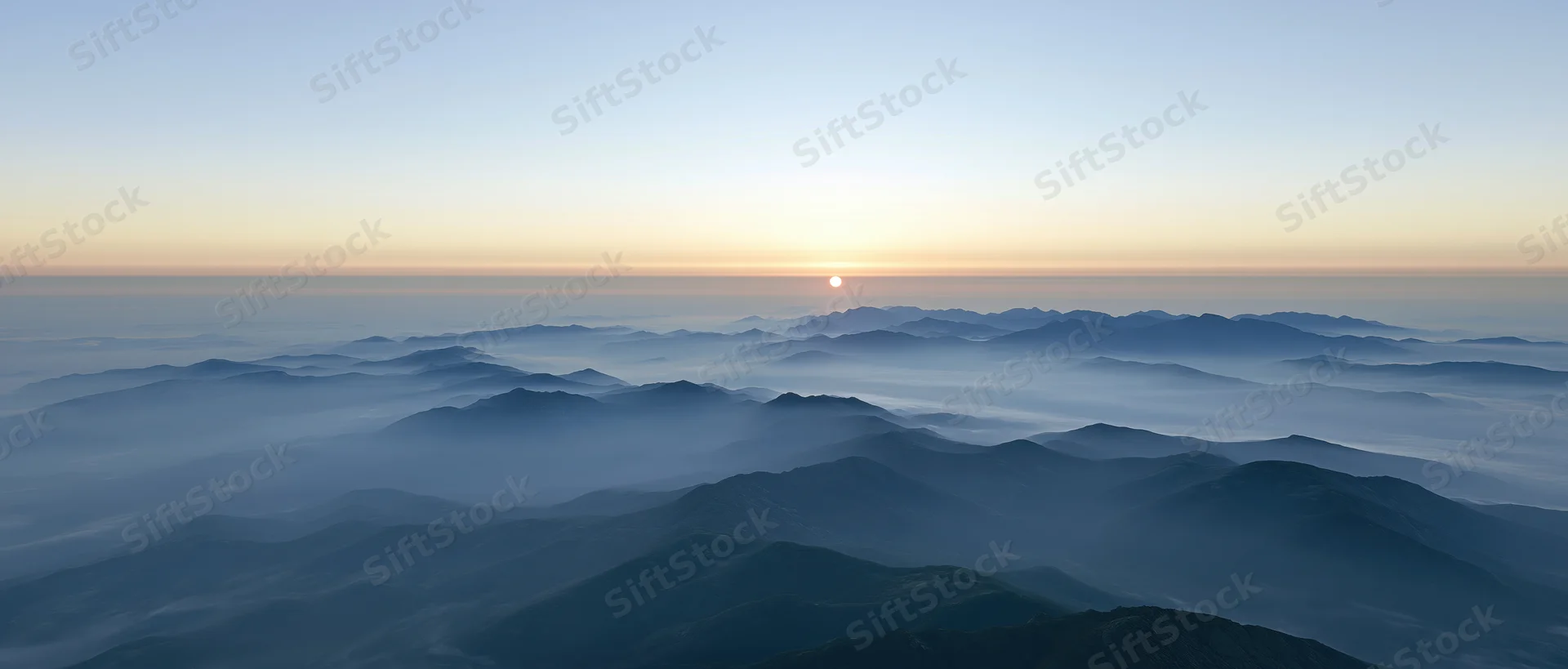 Aerial view of layered mountain ridges half-submerged in low mist at sunrise