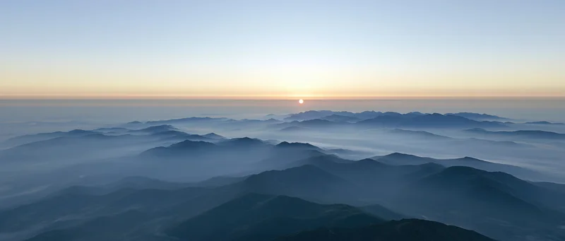 Aerial view of layered mountain ridges half-submerged in low mist at sunrise
