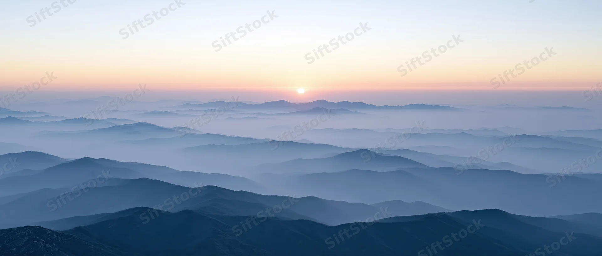 Aerial view of layered mountain ridges half-submerged in low mist at sunrise