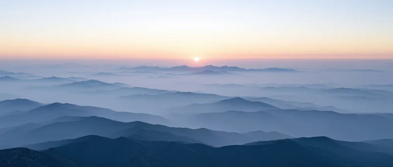 Aerial view of layered mountain ridges half-submerged in low mist at sunrise