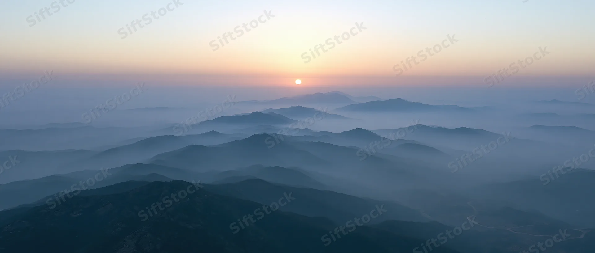 Aerial view of layered mountain ridges half-submerged in low mist at sunrise