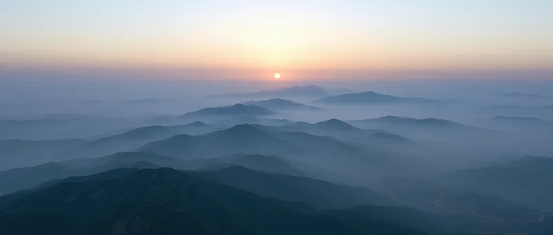 Aerial view of layered mountain ridges half-submerged in low mist at sunrise