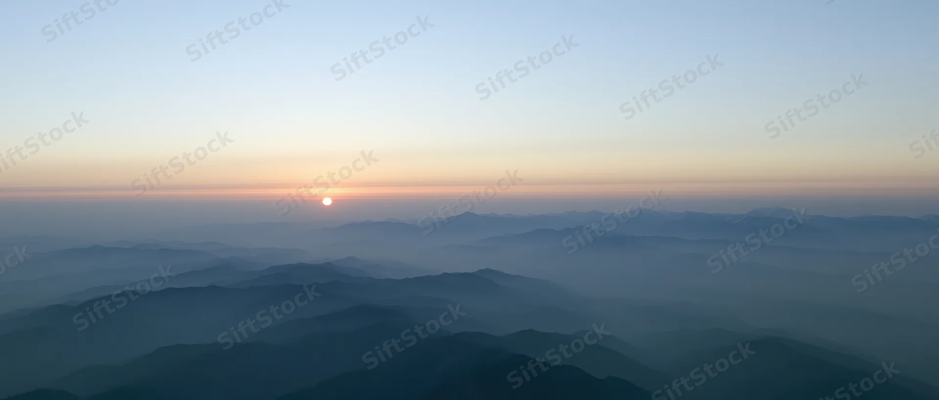 Aerial view of layered mountain ridges half-submerged in mist at sunrise