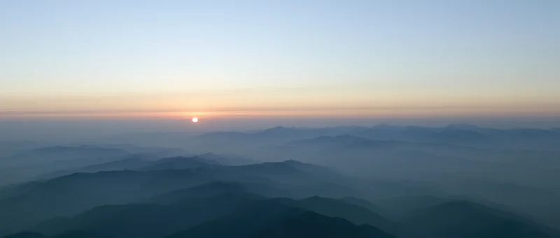 Aerial view of layered mountain ridges half-submerged in mist at sunrise