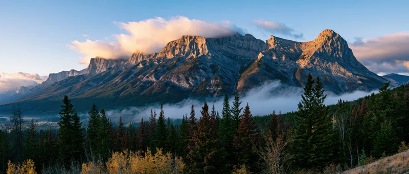 Alpine mountain range at sunset with mist in valley surrounded by pine forest in autumn