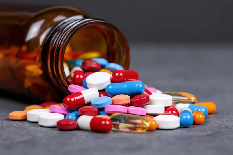 Scattered colorful pills and capsules spilling from an amber glass bottle on a dark surface