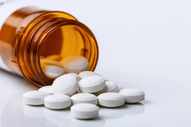 Amber prescription bottle tipped over with white pills spilled onto a white surface