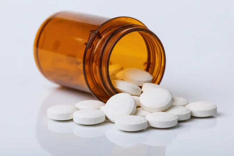 White pills spilling from an amber prescription bottle on a reflective white surface