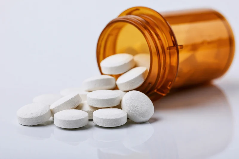 White pills spilling from an amber prescription bottle on a reflective surface