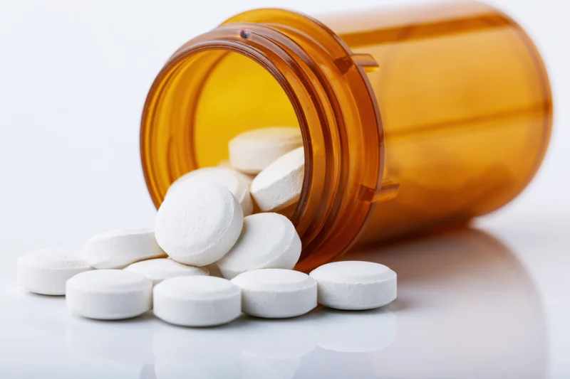 White tablets spilling from an amber prescription bottle on a reflective white surface