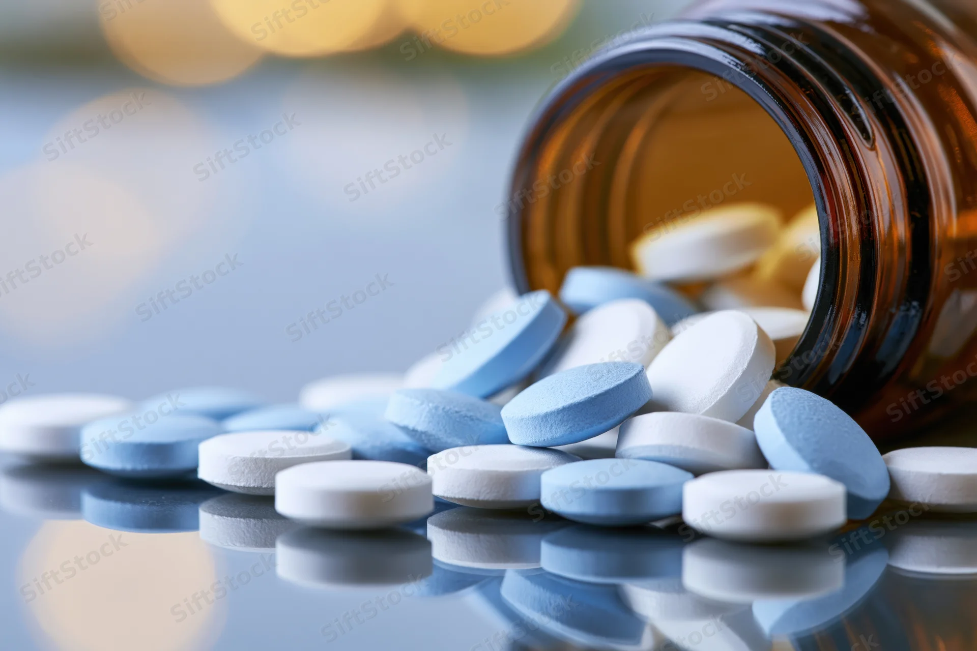 Spilled blue and white tablets from an amber glass prescription bottle on a reflective surface
