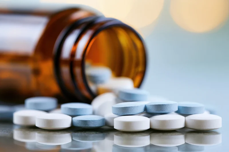 Spilled medication tablets from an amber glass bottle on a reflective surface