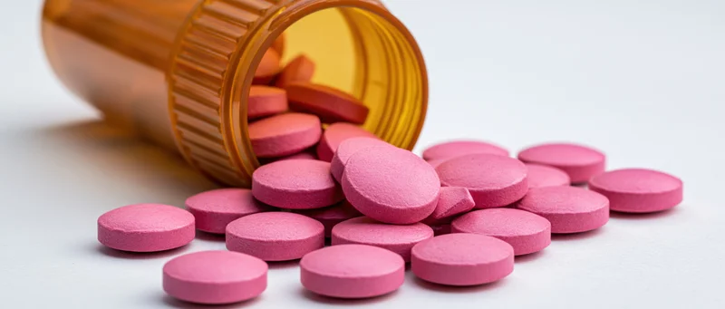 Pink pills spilling from an amber prescription bottle on a white surface