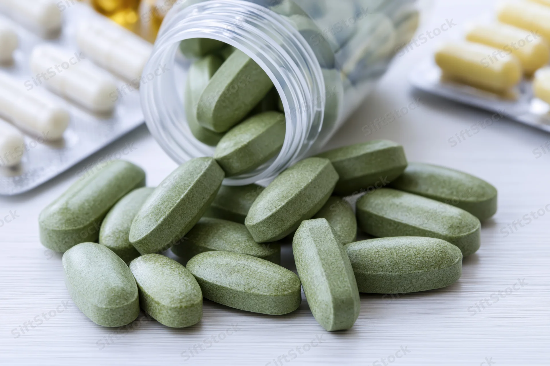Green pills spilled from a clear plastic bottle onto a white surface