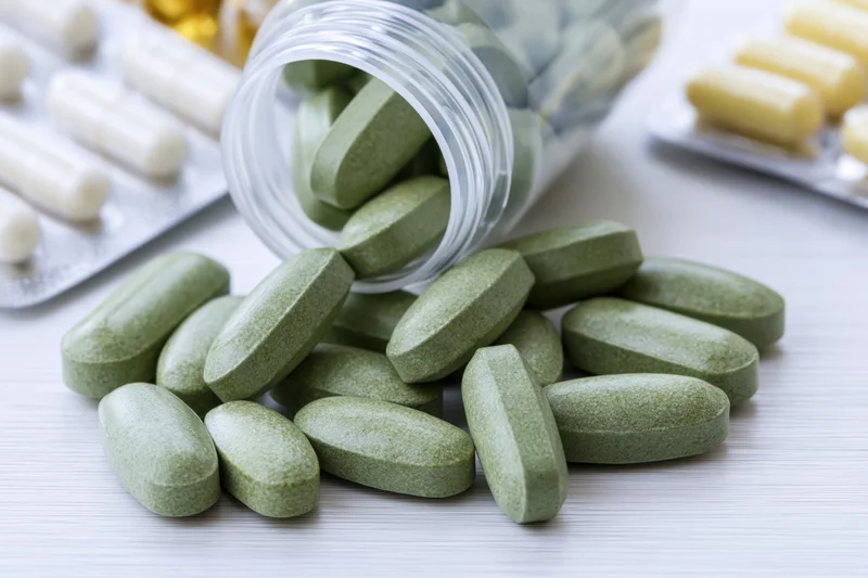 Green pills spilled from a clear plastic bottle onto a white surface