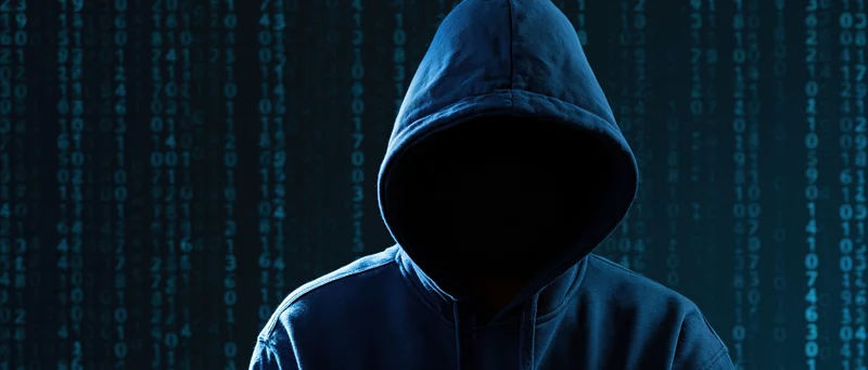 Hooded figure with hidden face standing before digital code display