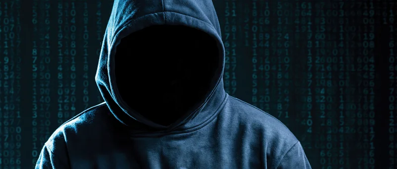 Hooded figure with hidden face standing before digital code display