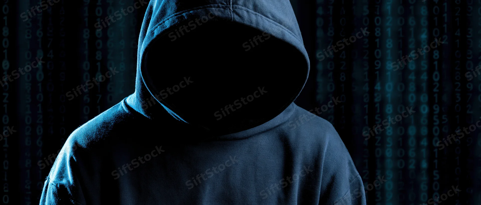 Hooded figure with hidden face standing before digital code background