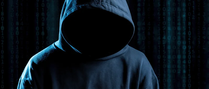 Hooded figure with hidden face standing before digital code background